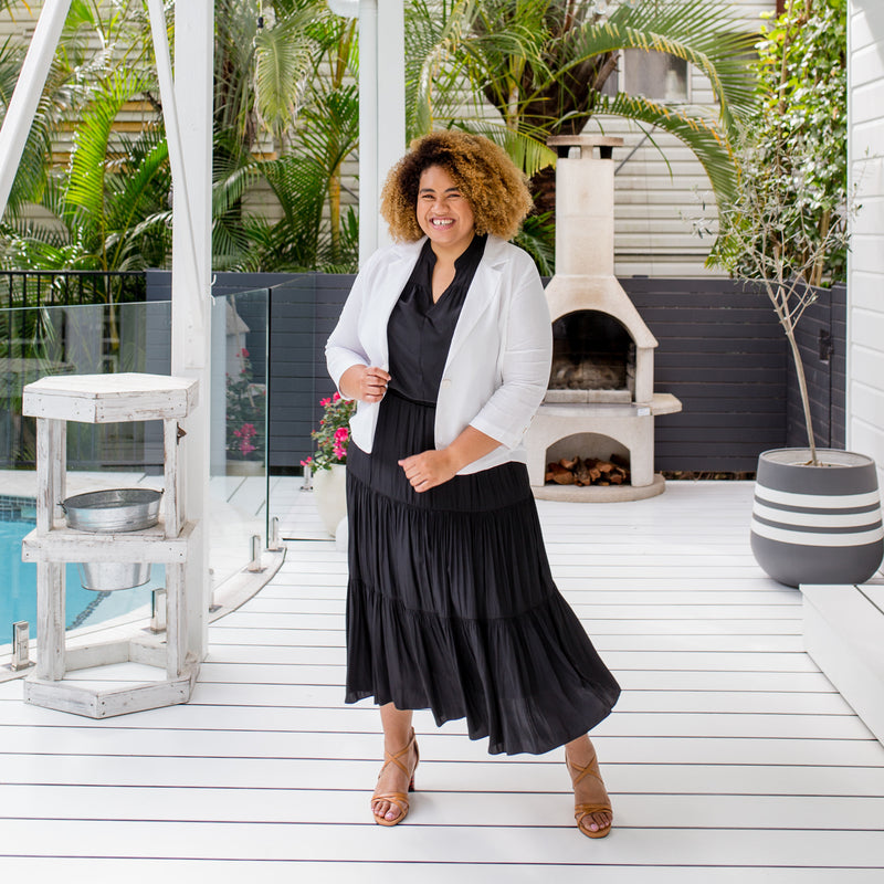 Asinate is wearing our Caroline linen blazer in white over  Stevie sleeveless blouse in black tucked into Sophie maxi skirt in black with tan sandals 