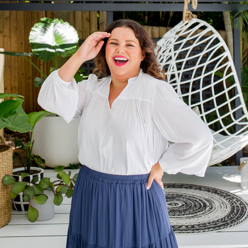 Stacey is wearing Felicity technical billow blouse in white tucked into  Sophie technical tiered maxi skirt in steel blue.