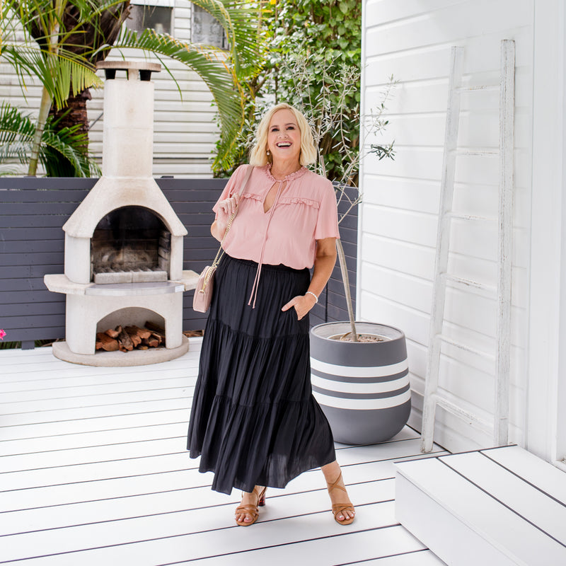 Nikki is wearing our Kim blouse in peach tucked into Sophie Maxi skirt in black with tan sandals and crossbody bag in milk tea